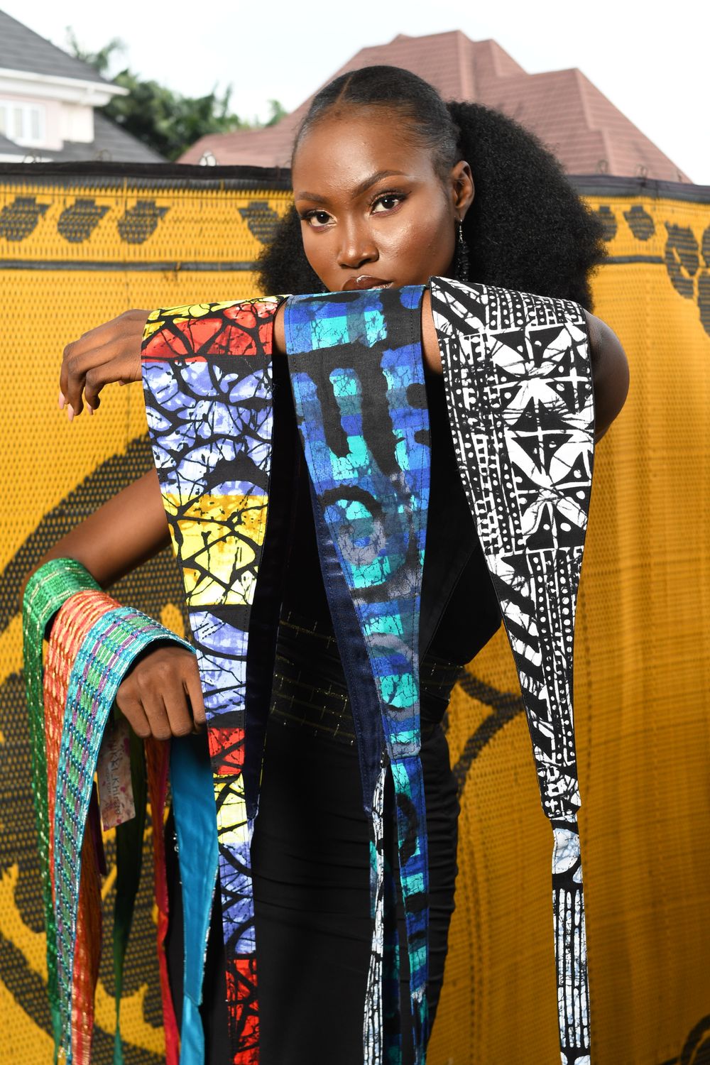 A model seated in a blue and gold patterned outfit against a yellow and black backdrop