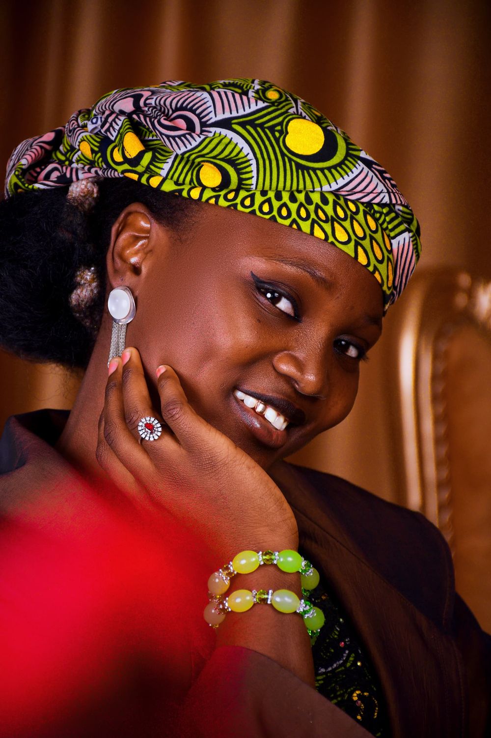 A smiling woman in a patterned headwrap and beaded necklace
